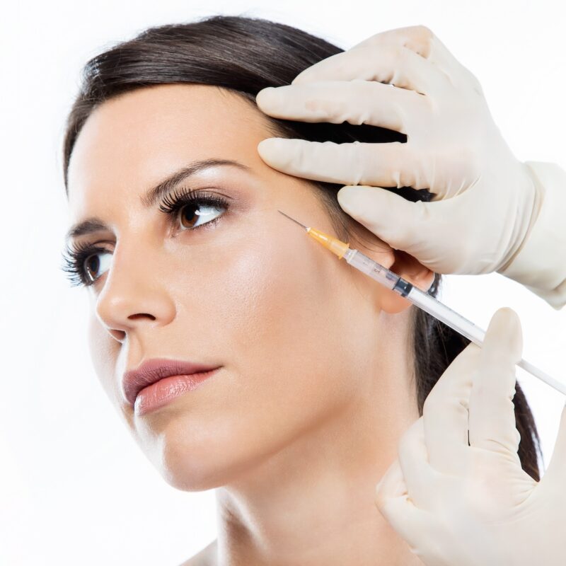 Portrait of beautiful young woman getting botox cosmetic injection in her face over white background.